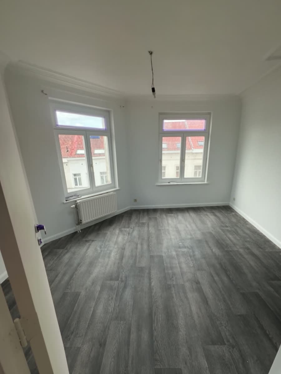 Séjour d'appartement rénové : murs repeints en blanc et nouveau sol en bois gris